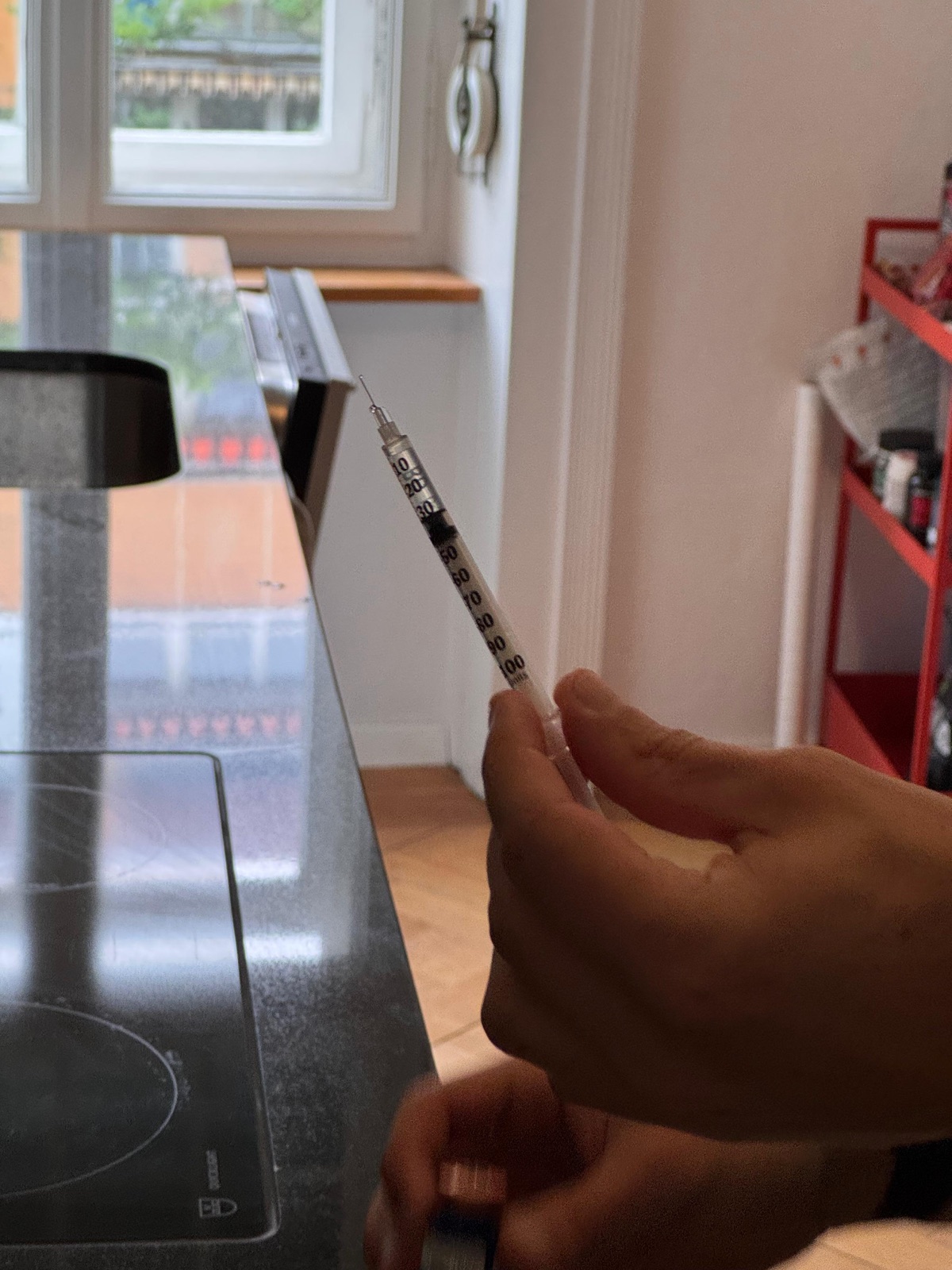 Hand holding an insulin syringe drawn up to a small dose in a kitchen