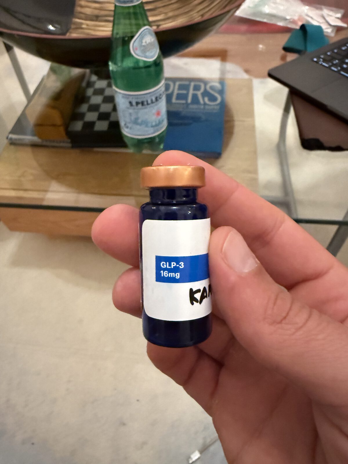 Hand holding a small dark glass vial labeled GLP-3 16mg with a handwritten marking